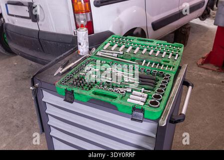 Organized green socket set on a rolling tool chest near a white van in a service bay, ready for vehicle maintenance. Stock Photo