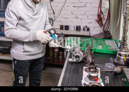 Technician wearing gloves works on a turbocharger using a tool at a workbench, surrounded by socket sets and engine parts. Stock Photo