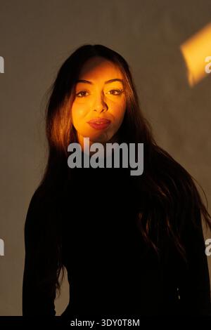 Woman standing in shadow with golden light illuminating one side of her face Stock Photo