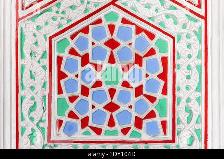 Handcrafted ornamental wall panel featuring white carved geometric and floral relief over vibrant green, red and blue painted background. Asian interi Stock Photo