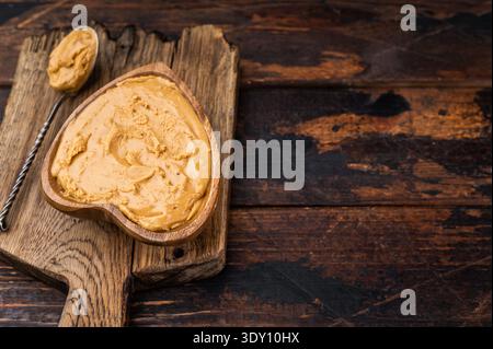 Creamy peanut butter spread in heart shaped wooden bowl on rustic cutting board with spoon. Natural peanut paste made from roasted peanuts Stock Photo
