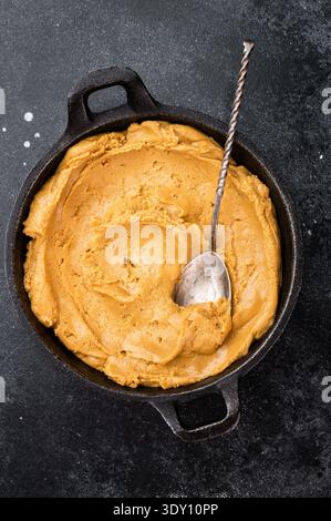 Smooth peanut butter spread in bowl with spoon on dark rustic background. Natural peanut paste made from roasted peanuts Stock Photo