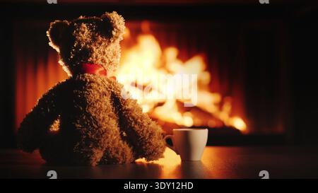 A bear cub with a cup of tea sits opposite the fireplace. Comfort and warmth in the house Stock Photo