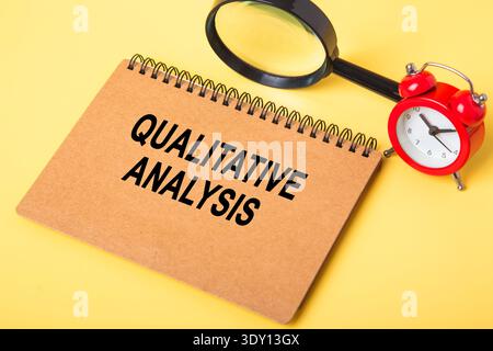 Notebook displaying qualitative analysis text with magnifying glass and alarm clock on yellow background Stock Photo