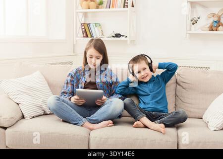Two kids listening music on couch at home Stock Photo