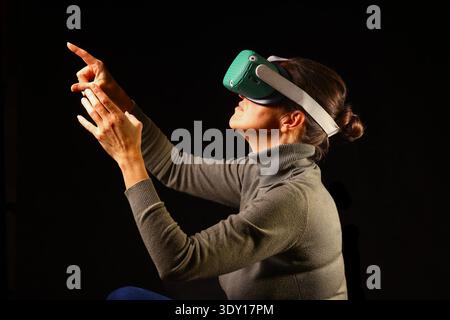 Woman reaching upward in a VR environment, captured in a side view that highlights curiosity, discovery and the excitement of exploring new digital po Stock Photo