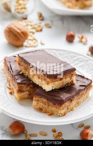 Homemade Vegan cocoa dates chocolate bars with coconut, hazelnuts, walnuts and sunflower seeds on a white background. Healthy dessert. The concept of Stock Photo