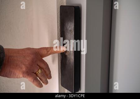 Close up of a senior woman hand pressing a silver doorbell, intercom button or elevator. Stock Photo
