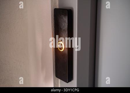 Close up of a modern silver elevator call button with glowing orange light ring. Stock Photo