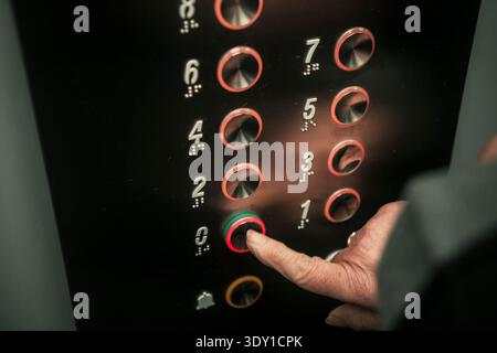 Close up of senior woman hand pressing an elevator button with braille numbers. Stock Photo