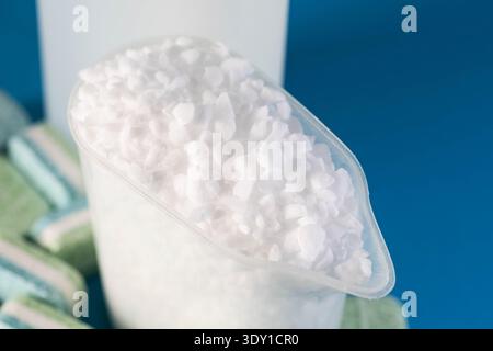Measuring cup of white granular dishwasher salt. Rinse aid bottle and cleaning tablets background. Dedicated products for dishwashing machines, spotle Stock Photo