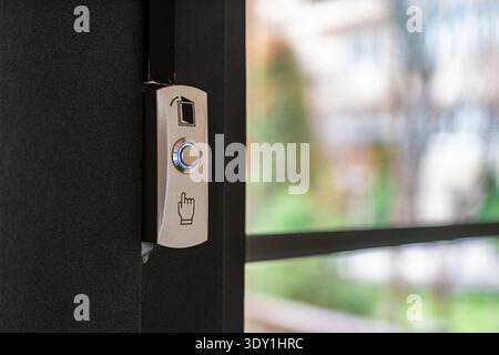 Close-up of a sleek doorbell button featuring a blue indicator light, designed for easy access. The background shows a blurred outdoor setting. Stock Photo
