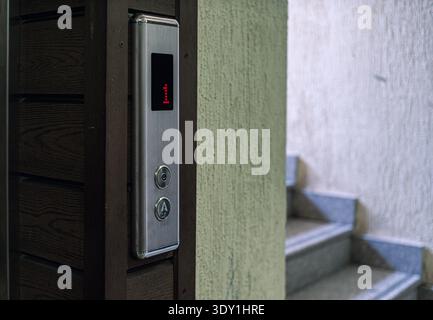 A close-up of an elevator control panel displaying the number one, with stairs visible in the background, highlighting a blend of modern and traditional architecture. Stock Photo