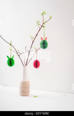 Colorful Easter eggs and spring twigs in vase against white wall Stock Photo