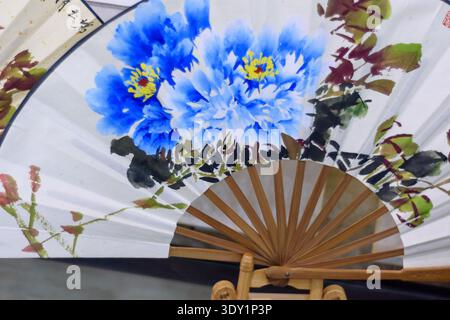 Bright watercolor floral painting of blue peonies on a decorative folding fan, wooden ribs visible Stock Photo
