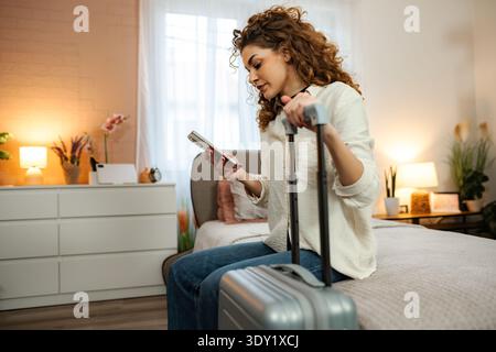Woman planning travel trip with mobile phone in bedroom Stock Photo