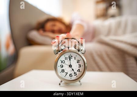 Woman hitting snooze button on alarm clock in morning Stock Photo