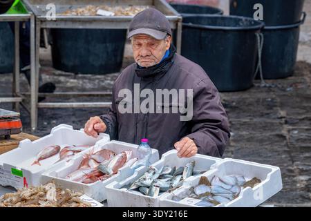 An older man selling fish at his stall in a fish market at Piazza Alonzo di Benedetto, Catania, Sicily, Italy. Stock Photo