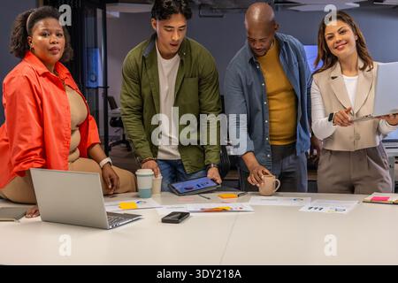 Diverse coworkers collaborating at conference table in business wear using laptop, tablet, papers. Team, collaboration, presentation, data, charts, gr Stock Photo