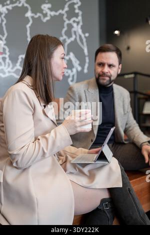 Colleagues talking and drinking coffee together at high wooden table in bright workspace. Coffee, talking, bright, workspace, teamwork. Stock Photo