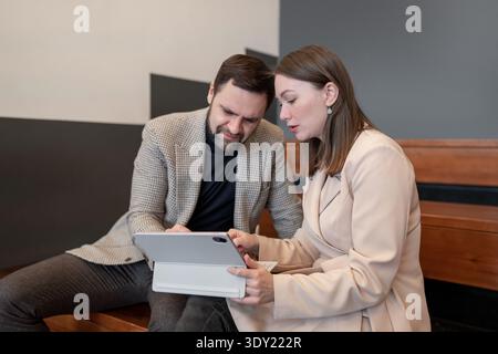 Business partners working side by side, looking at tablet and documents on wooden bench in office. Tablet, documents, bench, partnership, teamwork. Stock Photo
