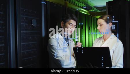 Reviewing laptop diagnostics, two engineers in white lab coats with eyeglasses in data center aisle. Server, racks, cabinet, cabling, hud, teamwork, m Stock Photo