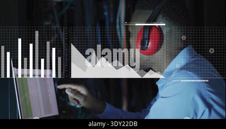 Pointing tech in light blue shirt, red headset, touching data-center screen with charts, copy space. Rack, cables, analytics, dashboard, monitoring, n Stock Photo