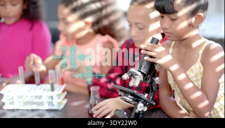 Examining girl in yellow dress peering into microscope at school table, with test tubes, copy space. Science, lab, students, teamwork, discovery, sunl Stock Photo