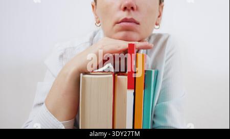 Learning Process. Tired Female Student Resting Chin on Stack of Colorful Books Looking at Camera Showing Academic Exhaustion and Study Stress in Schoo Stock Photo