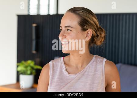 Woman smiling and looking left in lounge, wearing sleeveless pink top and gold hoops. Portrait, female, serenity, interior, plant, modern, warmth Stock Photo