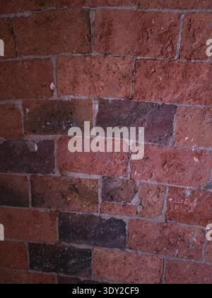 The photo shows a wall built with red bricks, characterized by porous texture with a rough and irregular surface and an aged appearance Stock Photo