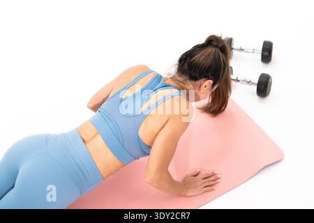 Woman exercises on pink mat. Dumbbells rest nearby, unused. Focused, determined posture shown. Ideal for fitness, wellness, or gym content. Clean back Stock Photo