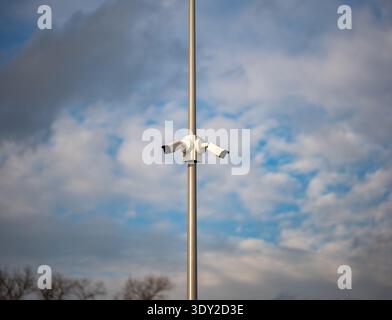 Modern CCTV security cameras on a tall pole against a cloudy blue sky Stock Photo