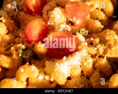 Golden pasta nestled in warm, cheesy embrace. Bright cherry tomatoes add vibrant pop of color. Crushed parmesan sparkles under golden light. Rich, com Stock Photo