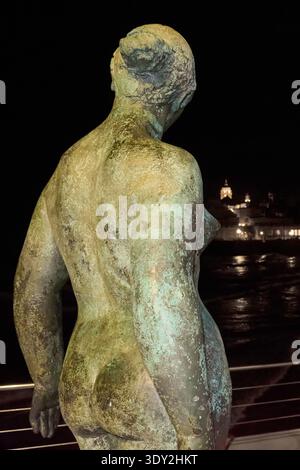 Sitges. Spain - March 05, 2026: Back view of the bronze statue Dona Mediterrania by Lluisa Granero facing the illuminated silhouette of the coastal to Stock Photo