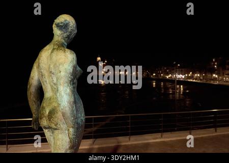 Sitges. Spain - March 05, 2026: Bronze sculpture Dona Mediterrania by Lluisa Granero overlooking the illuminated church of San Bartolome y Santa Tecla Stock Photo
