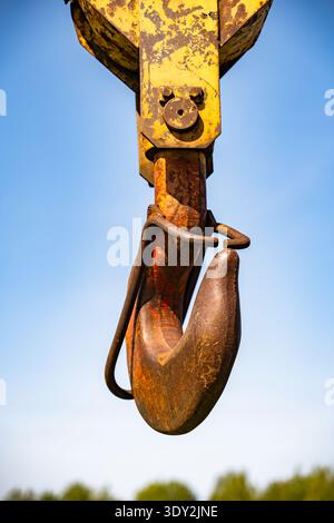 Old rusty industrial crane hook lifting heavy objects against a clear blue sky Stock Photo