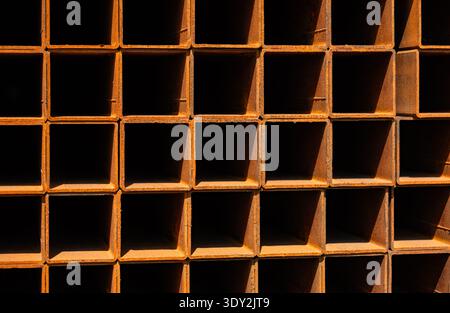 Rusty square metal pipes stacked, creating an industrial grid texture and pattern Stock Photo
