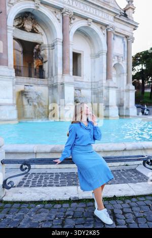 Stylish blonde woman standing by a famous fountain and classical architecture in Europe. Travel destination concept. Stock Photo