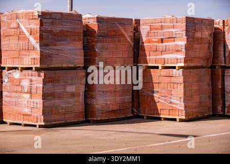 Stacks of red bricks on wooden pallets covered in plastic wrap for construction Stock Photo