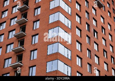 Modern building facade featuring red brick, many windows, and concrete balconies Stock Photo