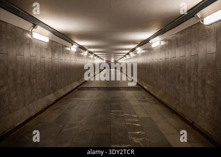 Long underground pedestrian tunnel extending with bright fluorescent lights leading forward Stock Photo