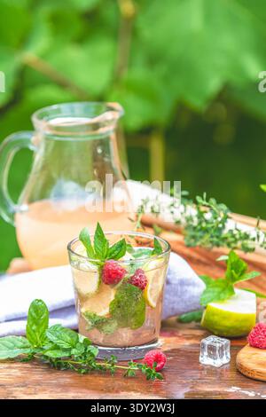 Raspberry mojito cocktail preparing on a rustic wooden table with fresh raspberries, lime wedges, and mint leaves, capturing the essence of a vibrant Stock Photo