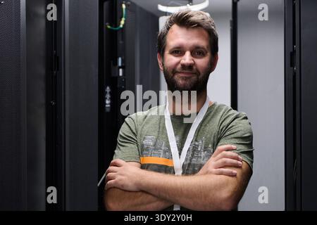 Confident IT engineer standing with arms crossed in a data center server room Stock Photo
