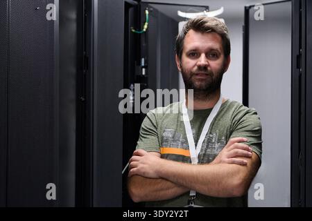 IT technician standing confidently in a data center server aisle with arms crossed Stock Photo