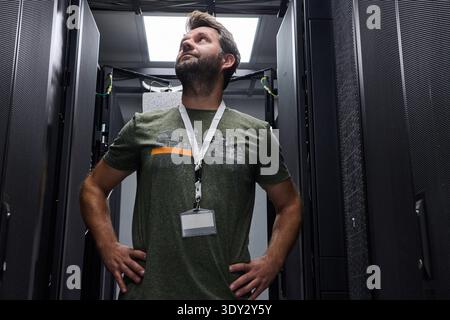 Confident IT technician inspecting server racks in a data center with hands on hips Stock Photo