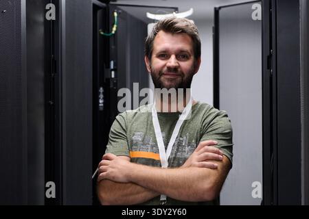 Confident IT technician standing with arms crossed in a data center server room Stock Photo