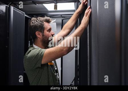IT technician inspecting server rack in data center performing maintenance and hardware installation Stock Photo