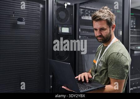 IT technician working on laptop in a data center server room managing network equipment and server racks Stock Photo