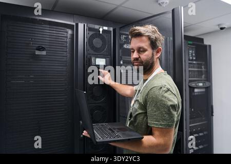 It technician working on servers in a data center with laptop checking rack equipment and controls Stock Photo